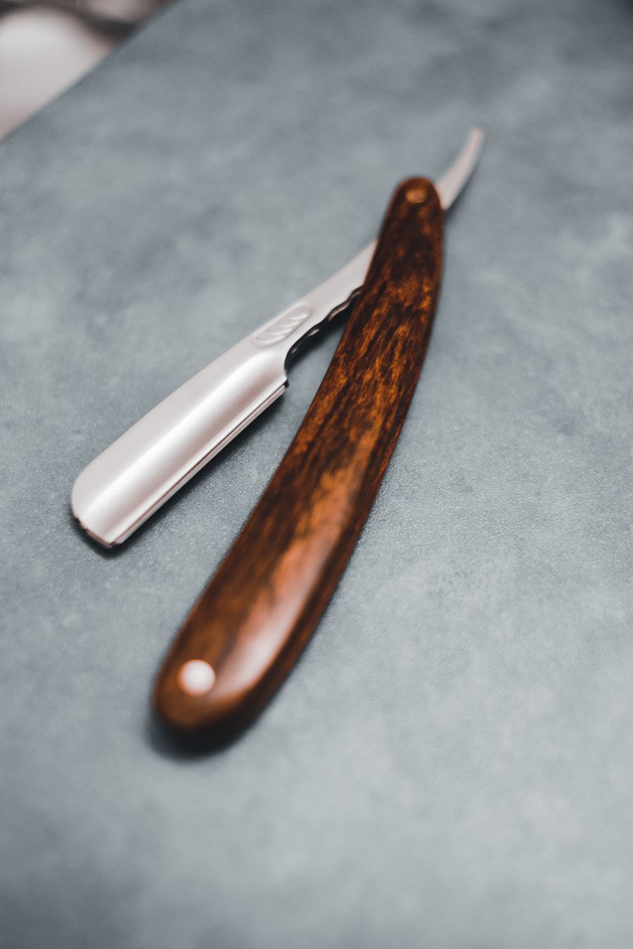 A straight razor with a wooden handle resting open on a stone counter