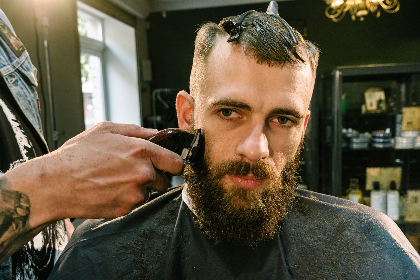 A barber lining up a client's fade with clippers in a dark, industrial-styled shop